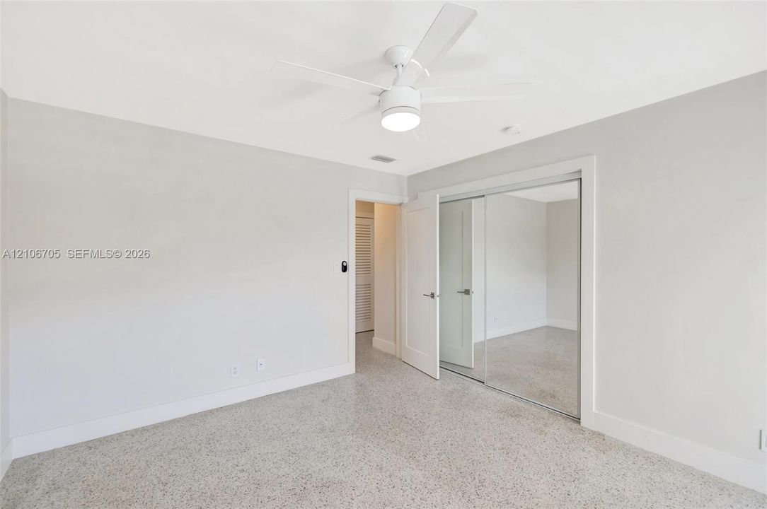 Neutral-toned interior featuring terrazzo flooring, a ceiling fan with integrated lighting, and a closet with mirrored sliding doors