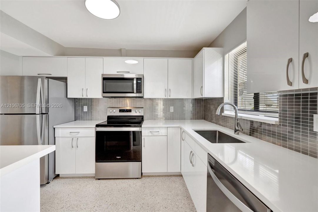 Kitchen featuring high-gloss white cabinetry, white stone countertops, stainless steel appliances, a mosaic tile backsplash, and a stainless steel undermount sink