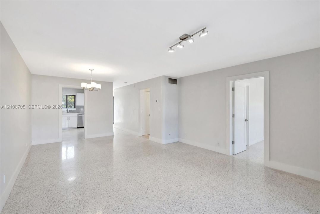 Open-concept interior featuring light-toned stone-composite flooring, neutral wall finishes, multi-directional track lighting, and a multi-light decorative chandelier
