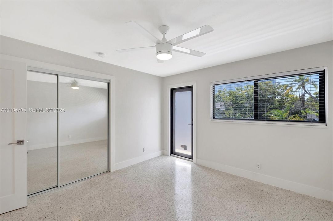 Terrazzo flooring, white ceiling fan with integrated lighting, dual-panel mirrored sliding closet doors, and single-lite exterior glass door