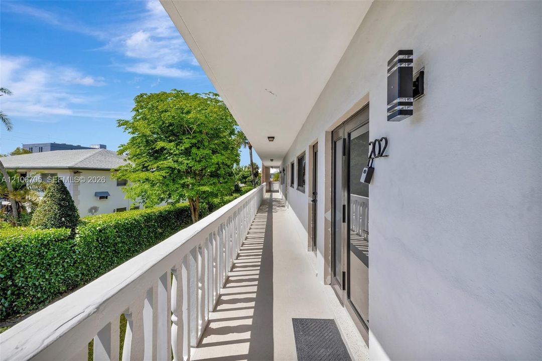 Exterior walkway featuring a white balustrade railing, smooth stucco walls, and dual-light modern wall sconces