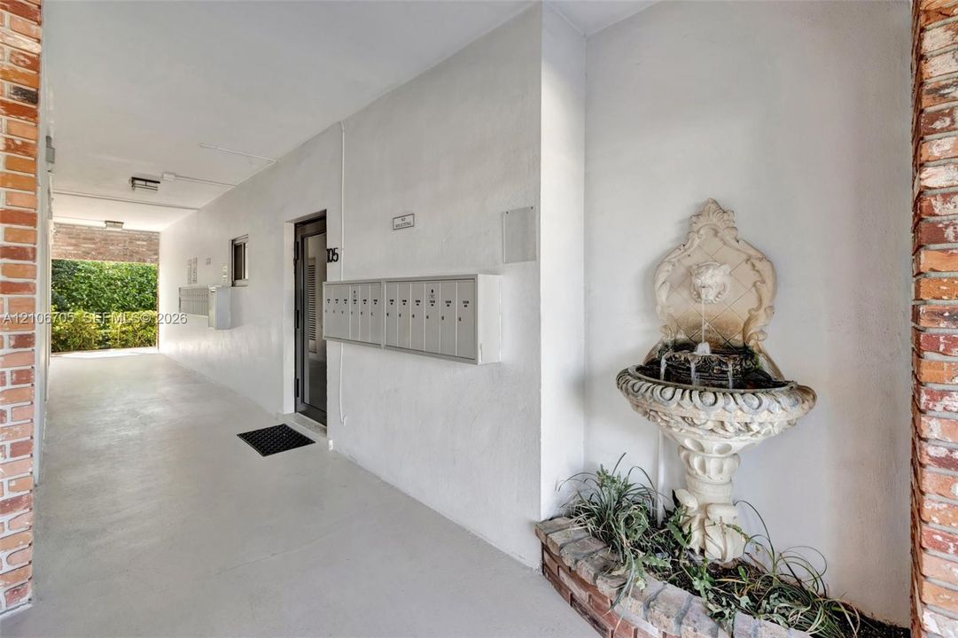 Covered exterior entryway featuring exposed brick columns, a decorative stone wall fountain, and integrated mailboxes