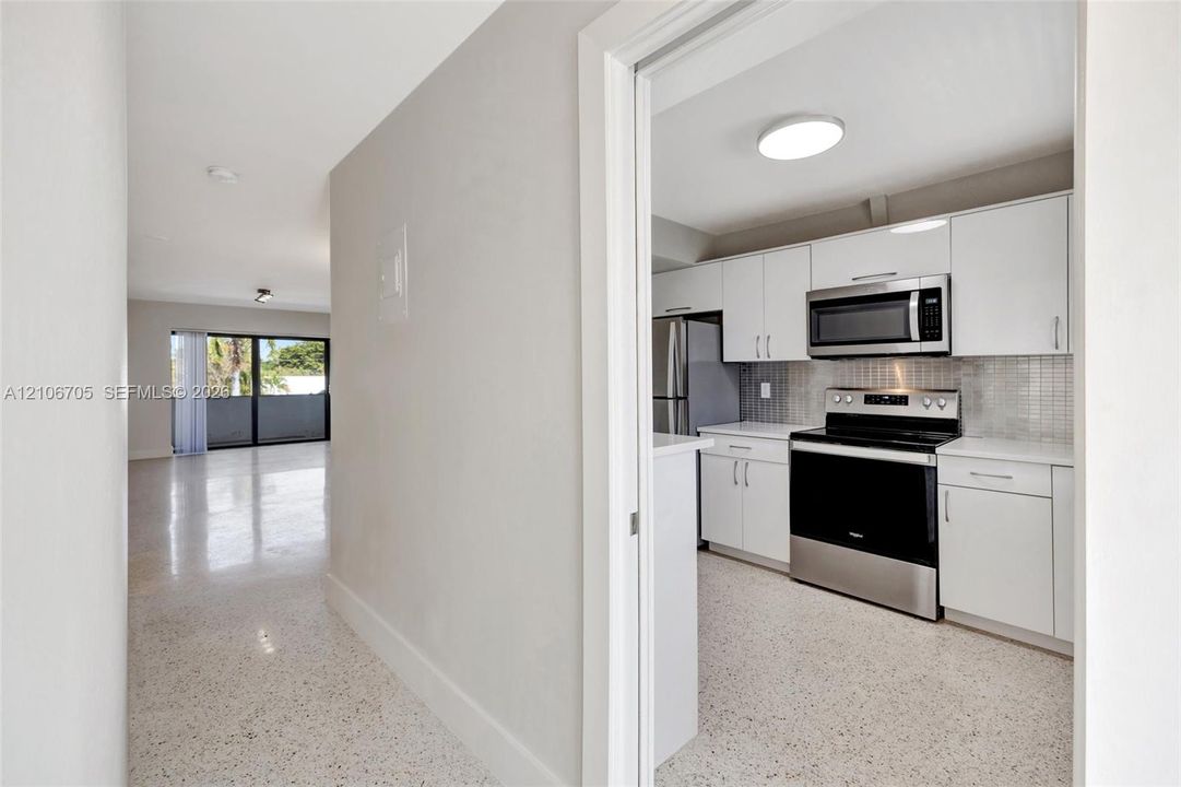 Kitchen featuring white shaker-style cabinetry, stainless steel appliances, and a tiled backsplash, finished with terrazzo flooring throughout