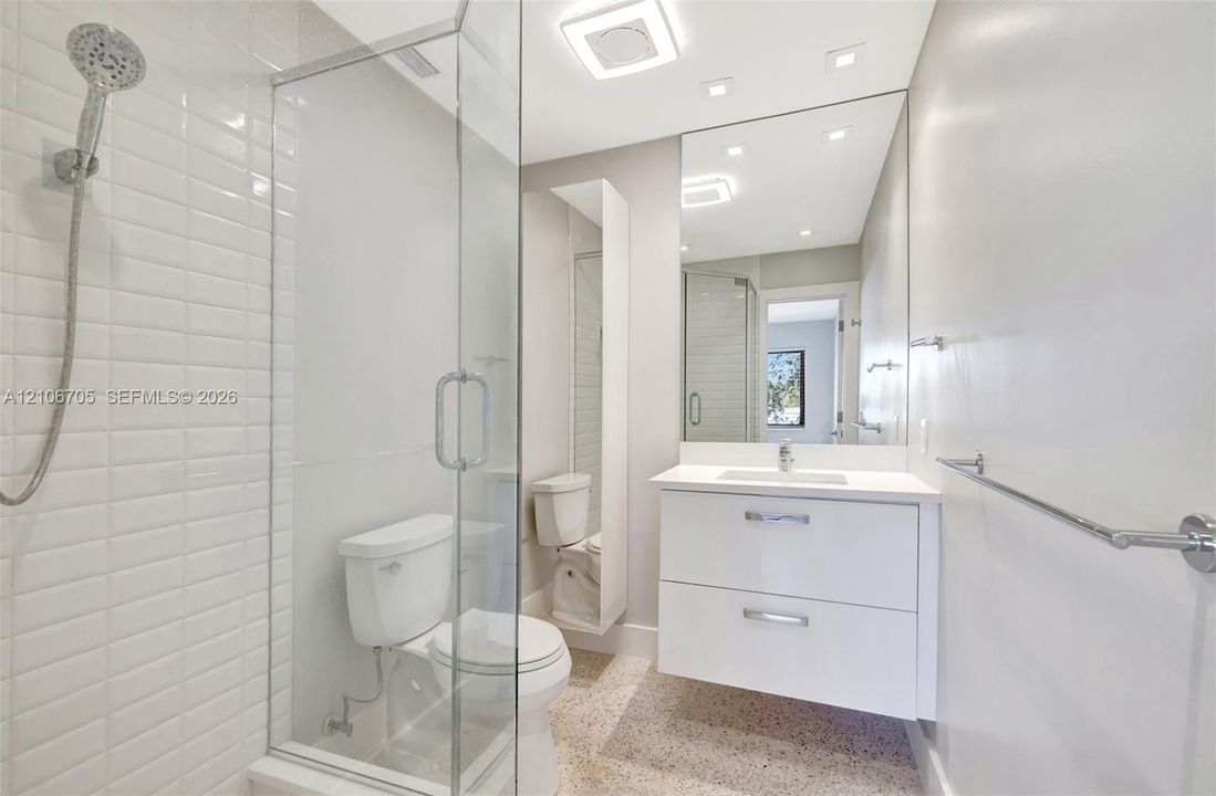 Bathroom featuring a white floating vanity with an integrated sink, a glass-enclosed shower with white subway tile surround, a large frameless mirror, and speckled flooring
