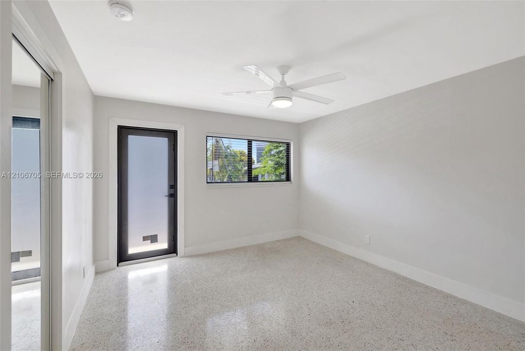 Polished terrazzo flooring, neutral wall finishes, black-framed door with frosted glass, horizontal window, and ceiling-mounted fan with integrated light