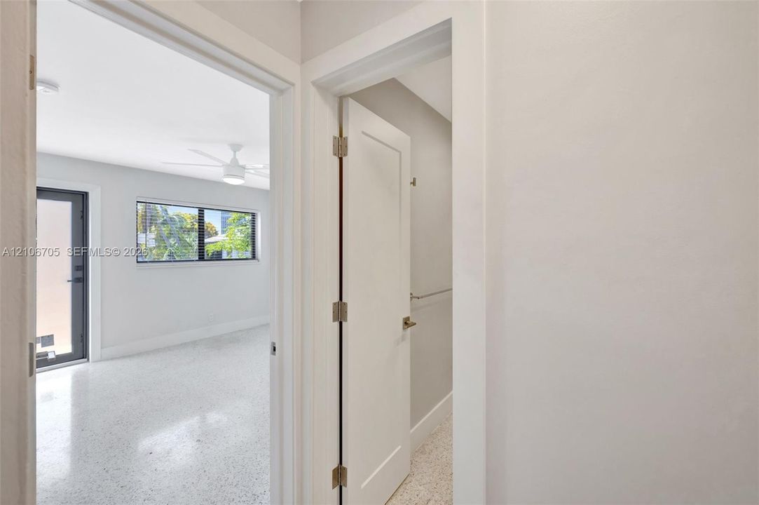 Interior space featuring terrazzo flooring, shaker-style door with matte hardware, multi-pane window with dark trim, ceiling fan with integrated lighting, and a glass-paneled exterior door