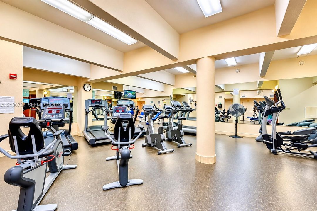 Fitness center featuring rubberized flooring, expansive wall-to-wall mirrors, recessed and flush-mount lighting, and structural support columns