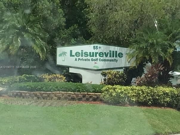 Community entrance monument featuring masonry landscaping borders, manicured shrubbery, and mature palm trees