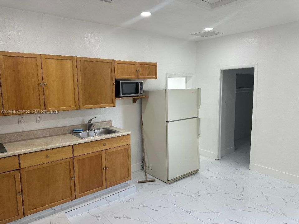 Kitchen featuring wood cabinetry, integrated countertops with a stainless steel sink, tile flooring, and recessed ceiling lighting