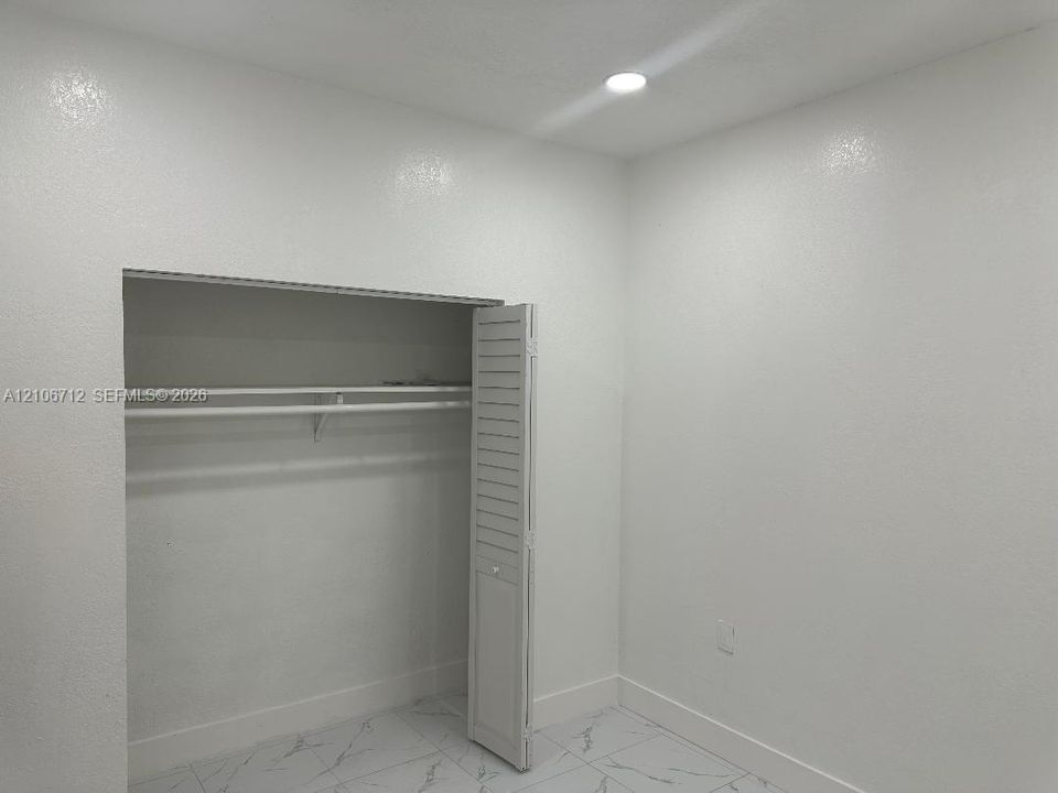 Room featuring white wall-finish, recessed lighting, tile flooring with marble-style veining, and a closet with louvered bifold doors