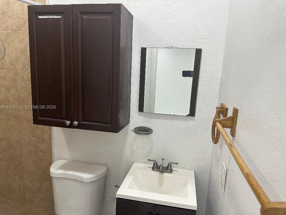 Dark wood-finish cabinetry, white vanity countertop with integrated sink, dual-handle metal faucet, wall-mounted mirror, and wall-mounted towel rack