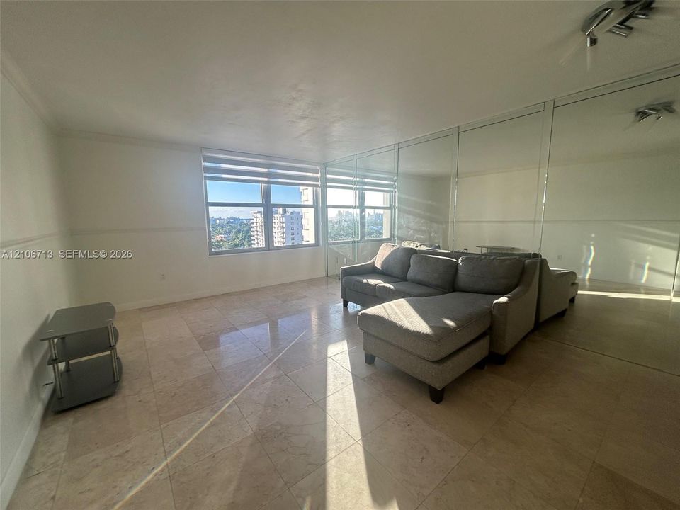 Living space featuring large-format tile flooring, wall-to-wall mirrored panels, and windows with integrated shades