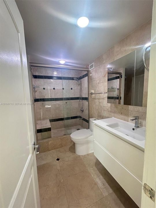 Bathroom featuring a modern floating vanity with an integrated sink, a walk-in shower enclosed by glass doors with decorative stone tile accents, and large-format stone tile flooring