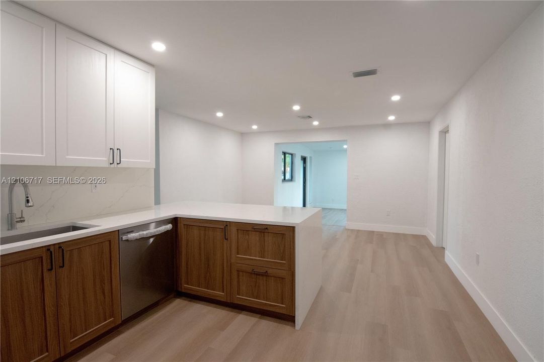 Kitchen featuring dual-tone shaker cabinetry, quartz countertops, stainless steel undermount sink with gooseneck faucet, integrated stainless steel dishwasher, and wood-finish flooring