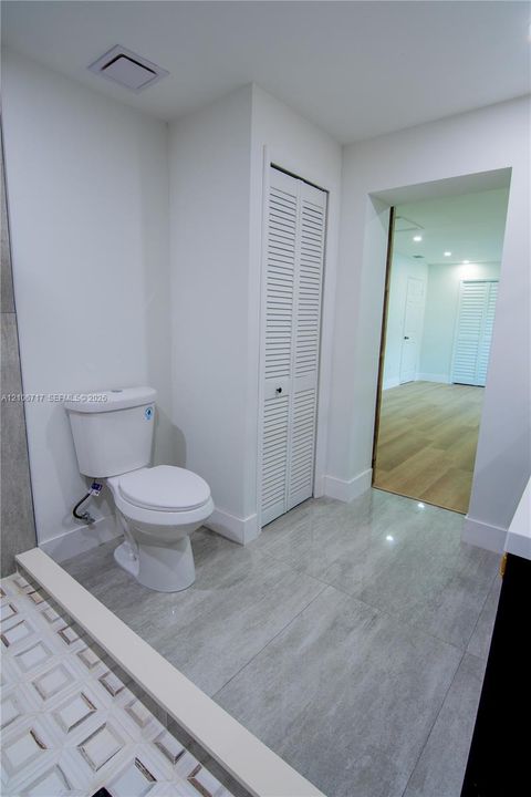 Bathroom featuring large-format ceramic tile flooring, a white porcelain toilet, and a closet with white louvered doors