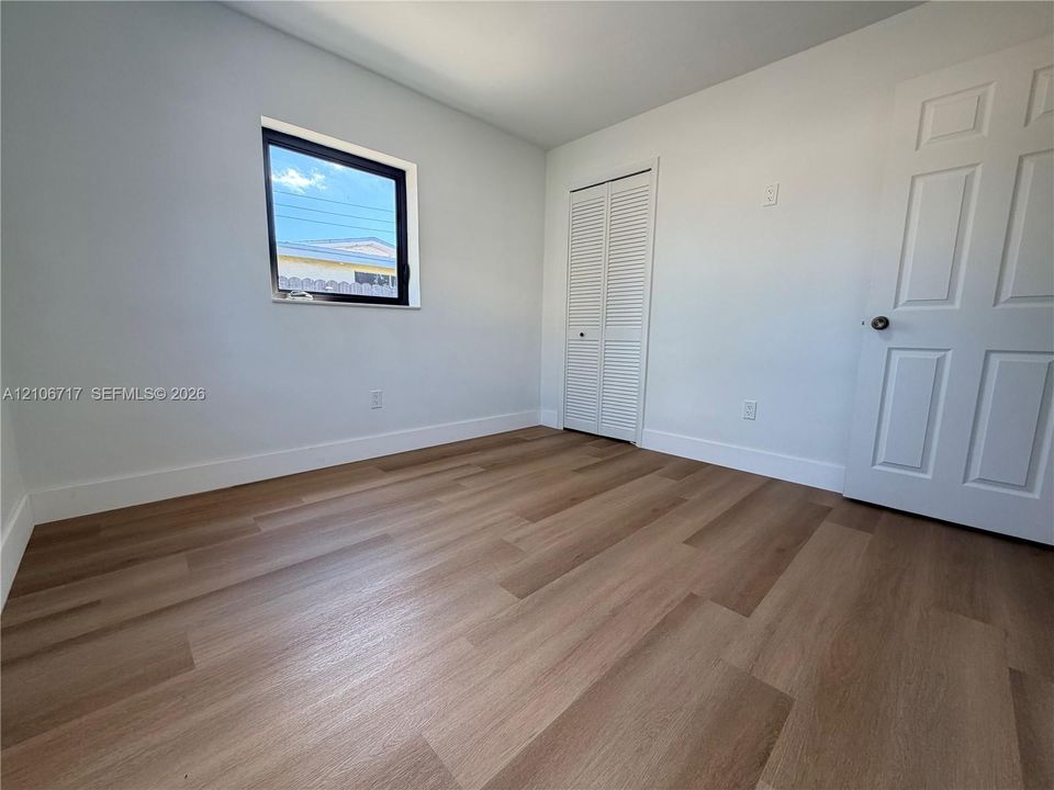 Wood-finish flooring, neutral wall tones, single-pane window, louvered-style closet doors, and a paneled interior door