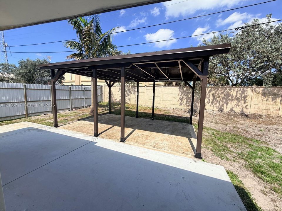 Covered carport featuring a structural timber frame, concrete slab, and privacy fencing