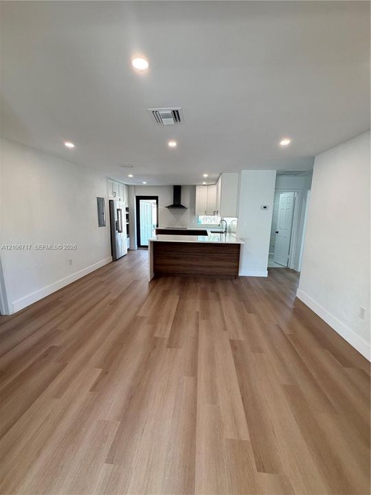 Open floor plan featuring wood-finish flooring, recessed lighting, white cabinetry, a kitchen island with a wood-tone base, and a wall-mounted chimney-style range hood
