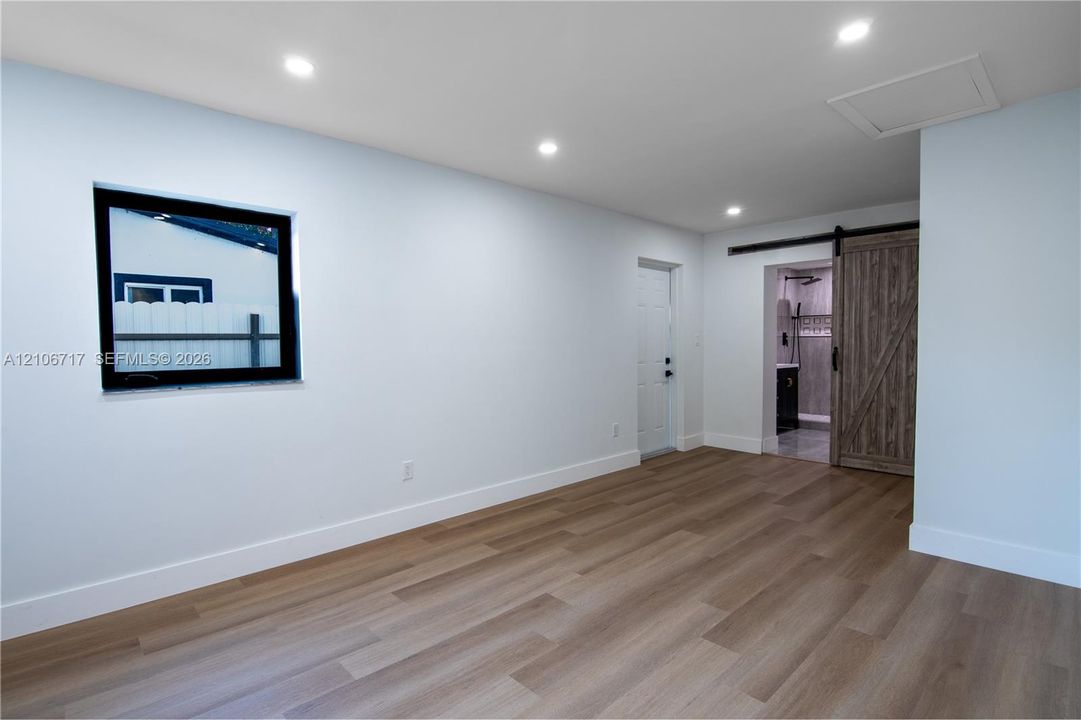 Neutral interior space featuring wood-finish flooring, recessed lighting, a single-hung window with a dark frame, and a sliding barn-style door