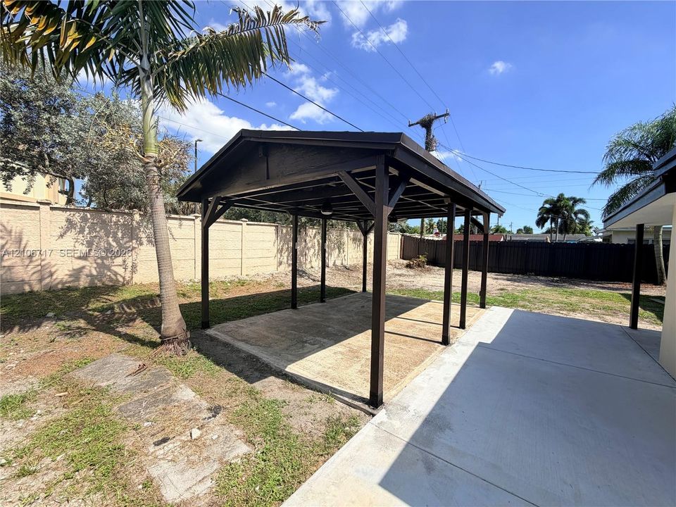 Covered gazebo featuring a dark-finish wood frame, concrete foundation, and high-contrast roof, situated within a fenced exterior space