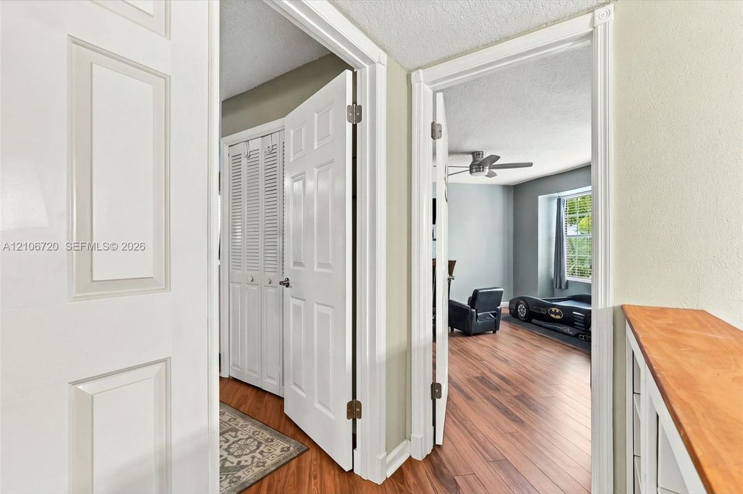Interior space featuring wood-finish flooring, white paneled doors, louvered bi-fold closet doors, a built-in wooden shelving unit, and a ceiling fan