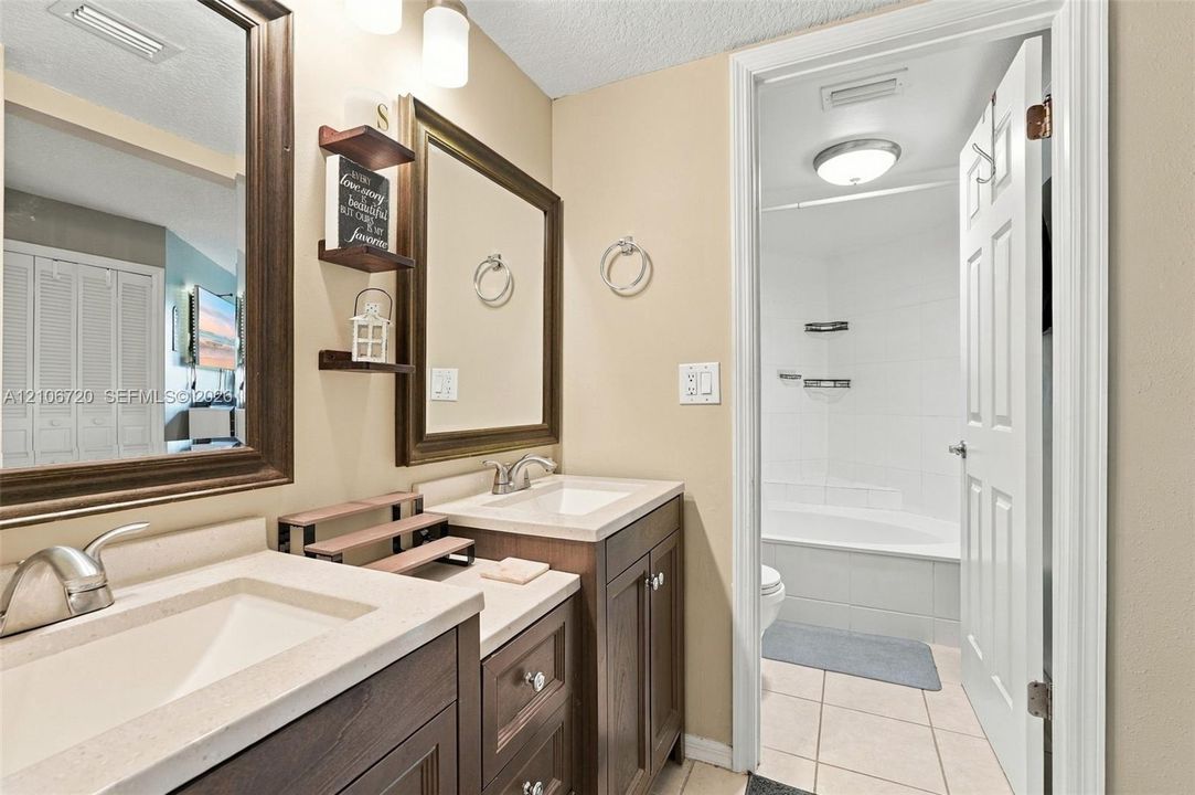 Double vanity with quartz countertops, integrated rectangular sinks, wood-finish cabinetry, framed mirrors, and a tile-surround bathtub