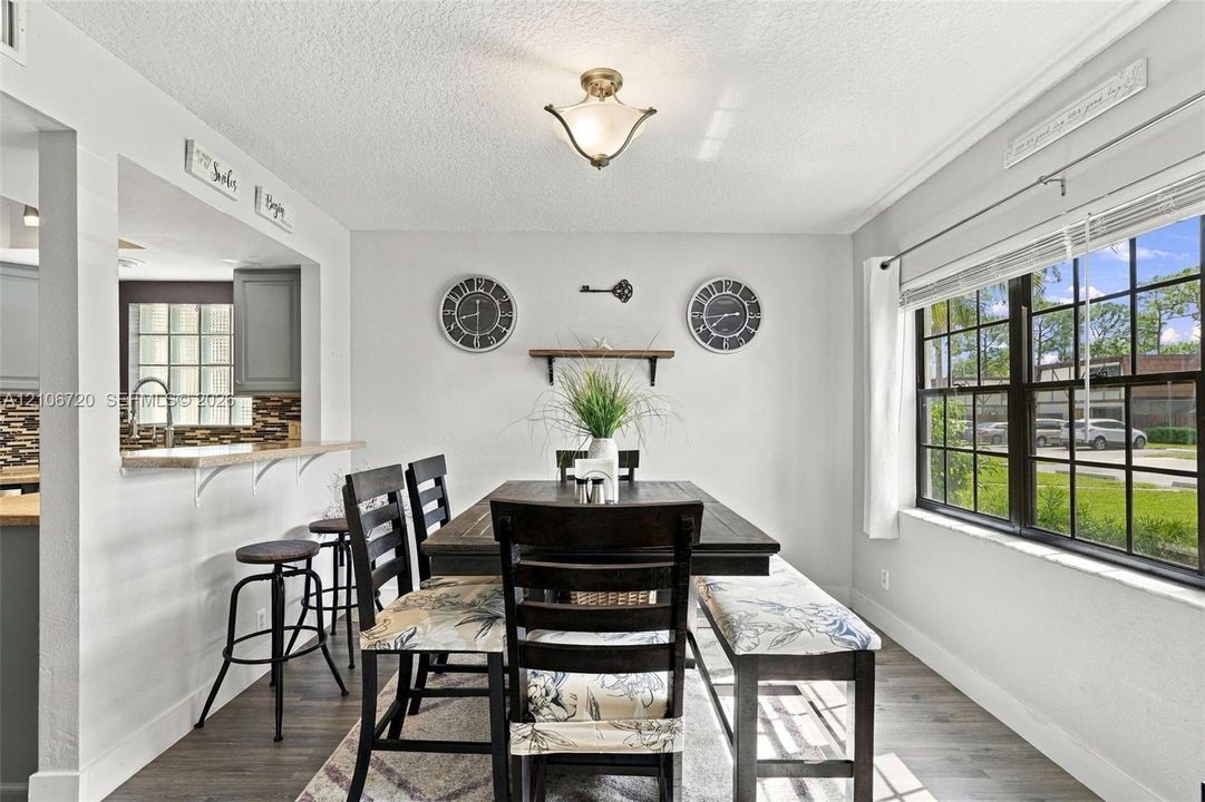 Dining area featuring wood-finish flooring, a pass-through window with a breakfast bar, and a multi-pane window with natural lighting