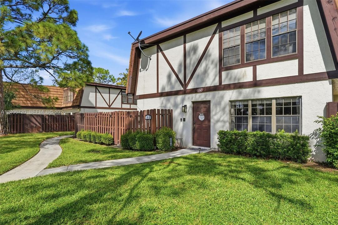 Tudor-style exterior featuring stucco facade with timber framing, multi-pane windows, a private fenced entry courtyard, and mature landscaping
