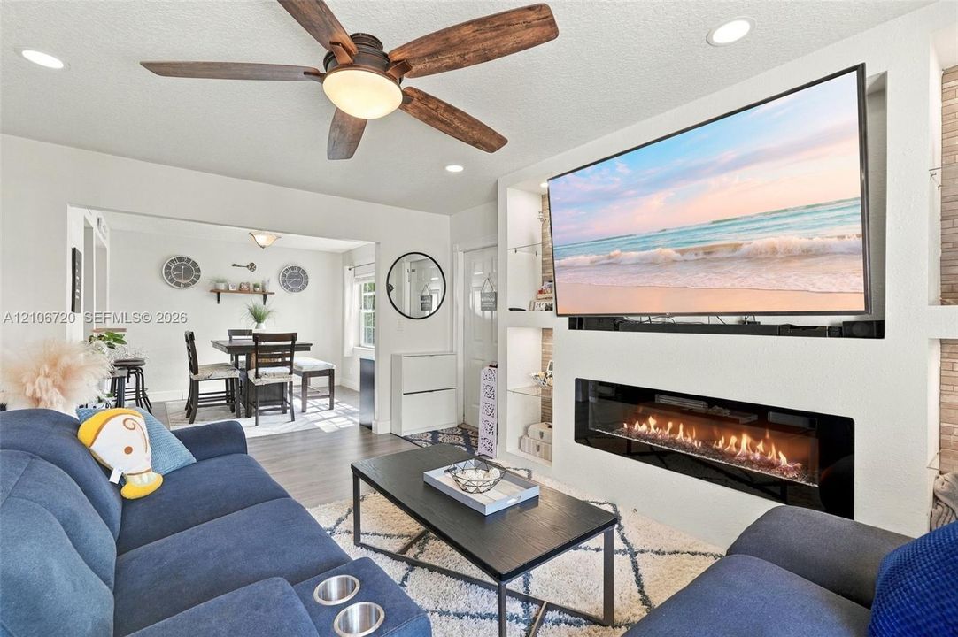 Built-in media wall featuring a linear electric fireplace, recessed shelving with glass inserts, recessed lighting, and a multi-blade ceiling fan