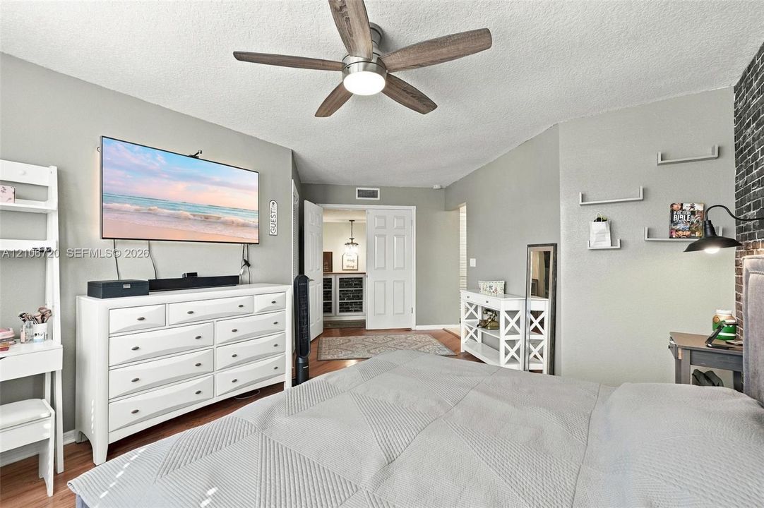 Neutral-toned bedroom featuring a dark brick-veneer accent wall, multi-shelf wall-mounted organizers, and a central ceiling fan with integrated lighting