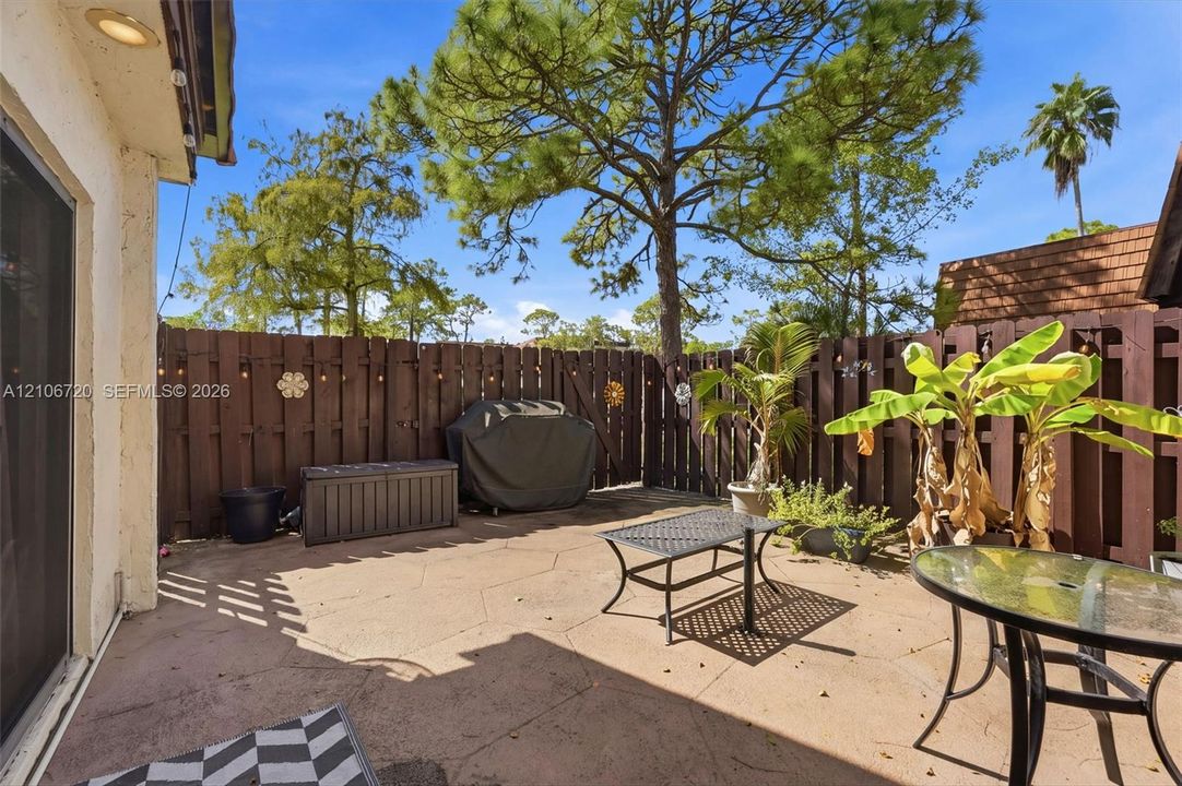 Private patio featuring a concrete paver surface, enclosed by a solid wood privacy fence and mature landscaping