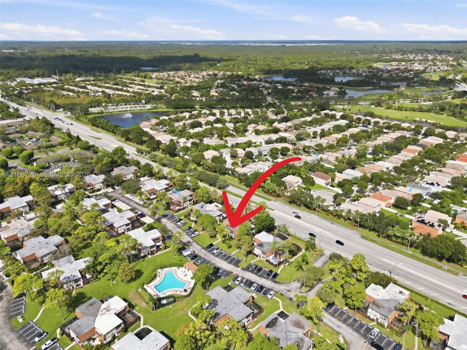 Aerial perspective of a multi-unit residential community featuring mature landscaping and a centrally located outdoor swimming pool