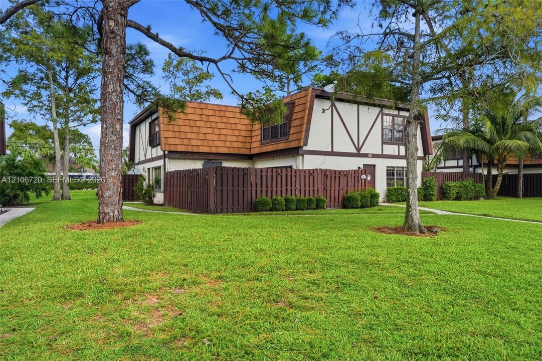 Two-story residence featuring a mansard roof, exterior timber framing, integrated wood privacy fencing, and mature pine trees on the grounds