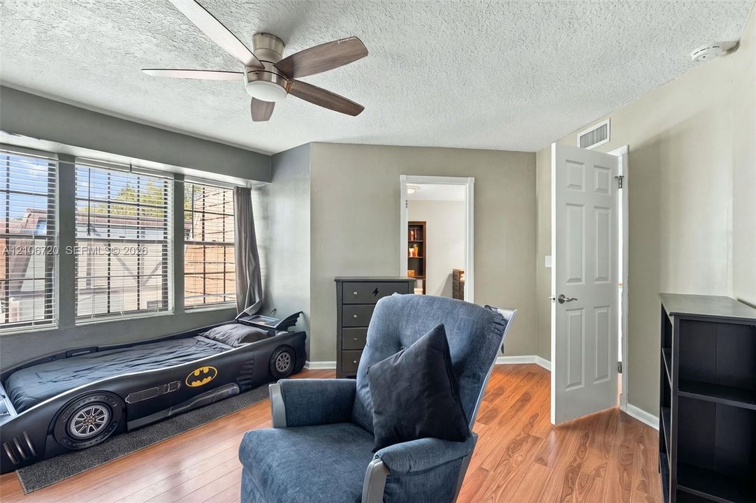 Room featuring wood-finish flooring, a multi-pane bay window, and a ceiling fan with integrated lighting