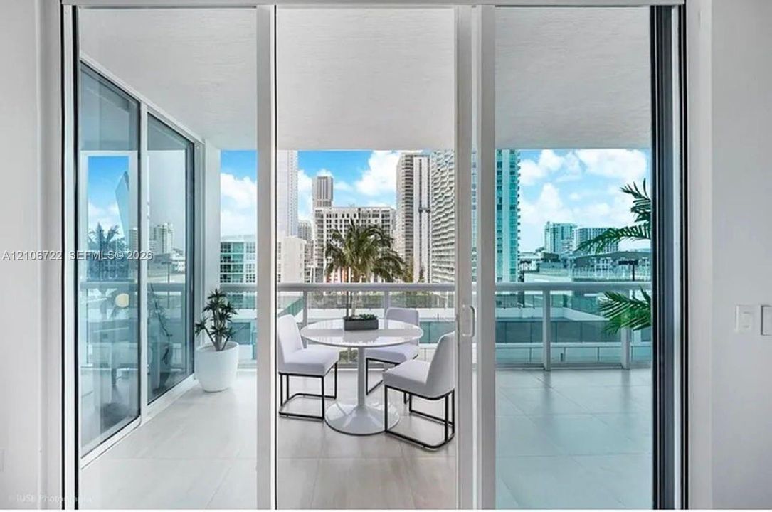 Covered balcony featuring oversized floor-to-ceiling sliding glass doors, neutral tile flooring, and a glass-paneled railing