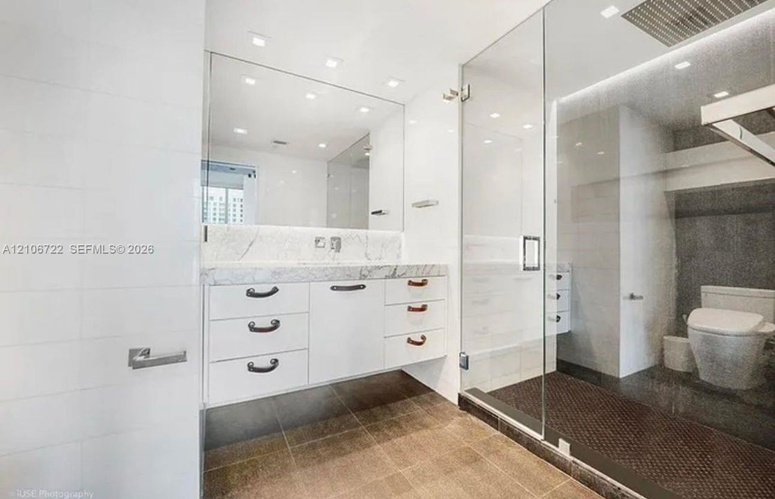 Floating white vanity featuring a stone countertop, wall-to-wall mirror, glass-enclosed shower, recessed ceiling lighting, and large-format floor tiling