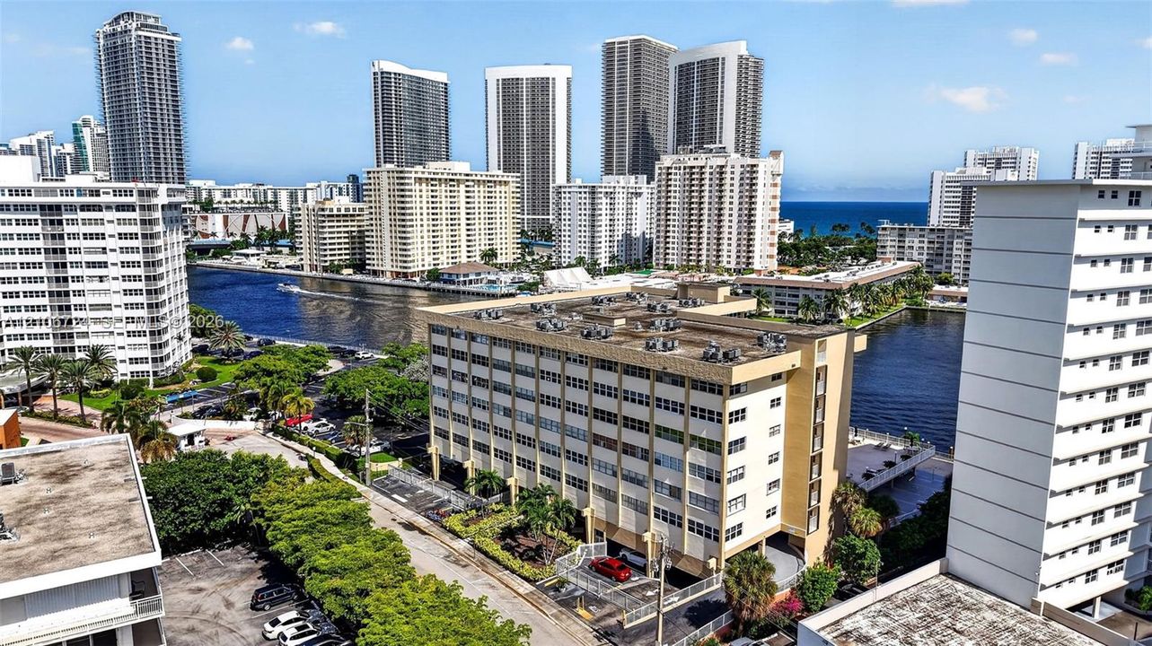 Mid-rise multi-story building featuring a concrete facade, flat roof with roof-mounted HVAC units, ground-level covered parking, and an urban waterfront location
