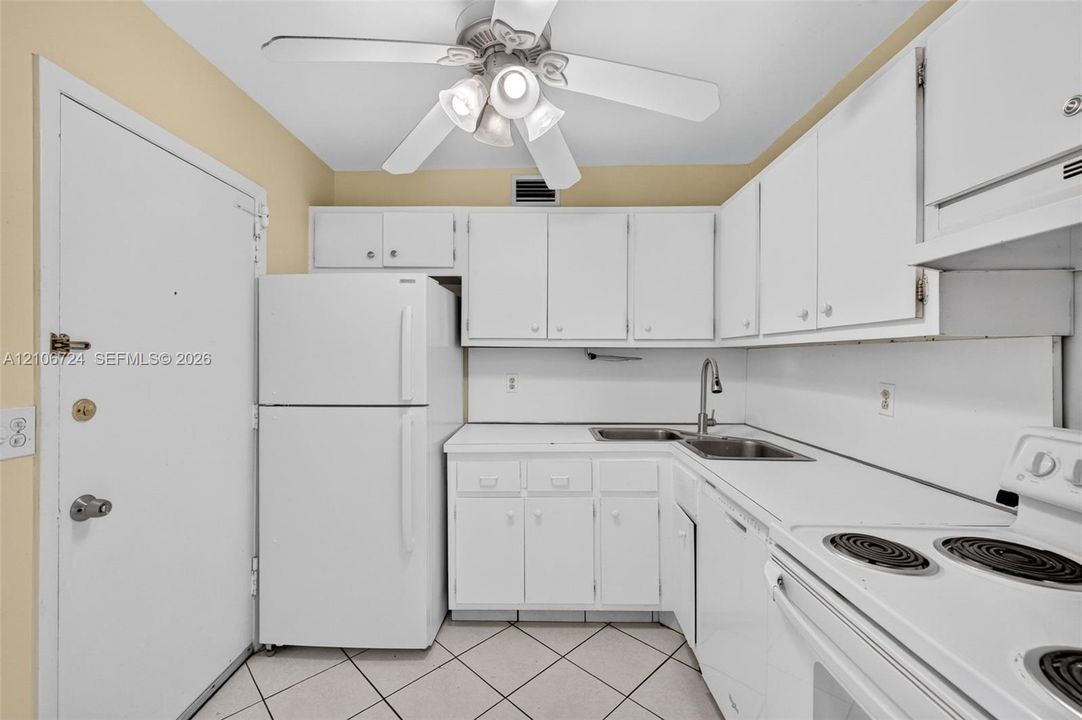 Kitchen featuring white cabinetry, solid-surface countertops, dual-basin stainless steel sink with high-arc faucet, white appliances, and a ceiling-mounted light fixture with fan