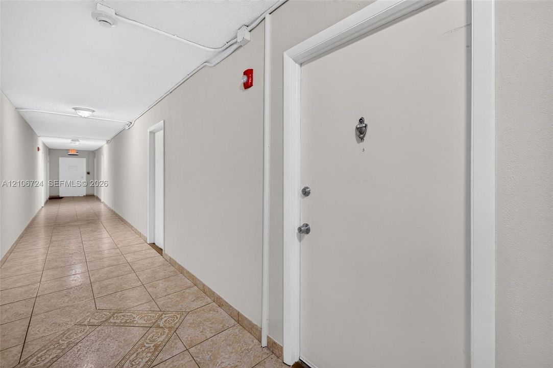 Interior corridor featuring tile flooring with decorative inlay, solid-core doors, and recessed ceiling lighting