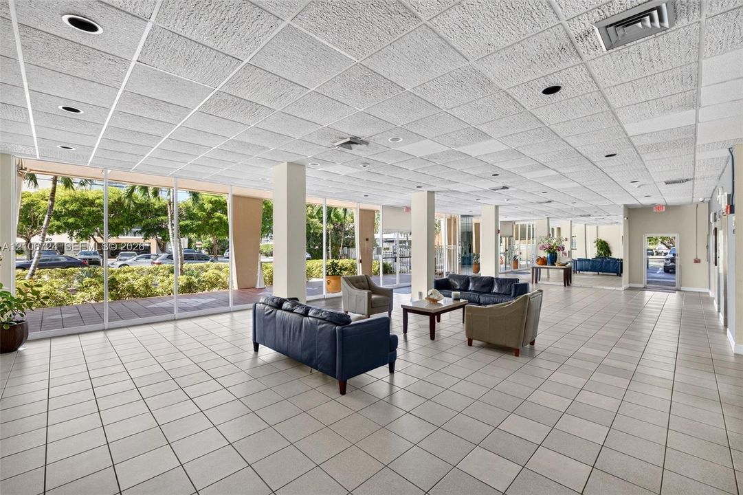 Open-concept interior featuring floor-to-ceiling glass panel walls, square ceramic tile flooring, recessed lighting, and a drop-grid ceiling