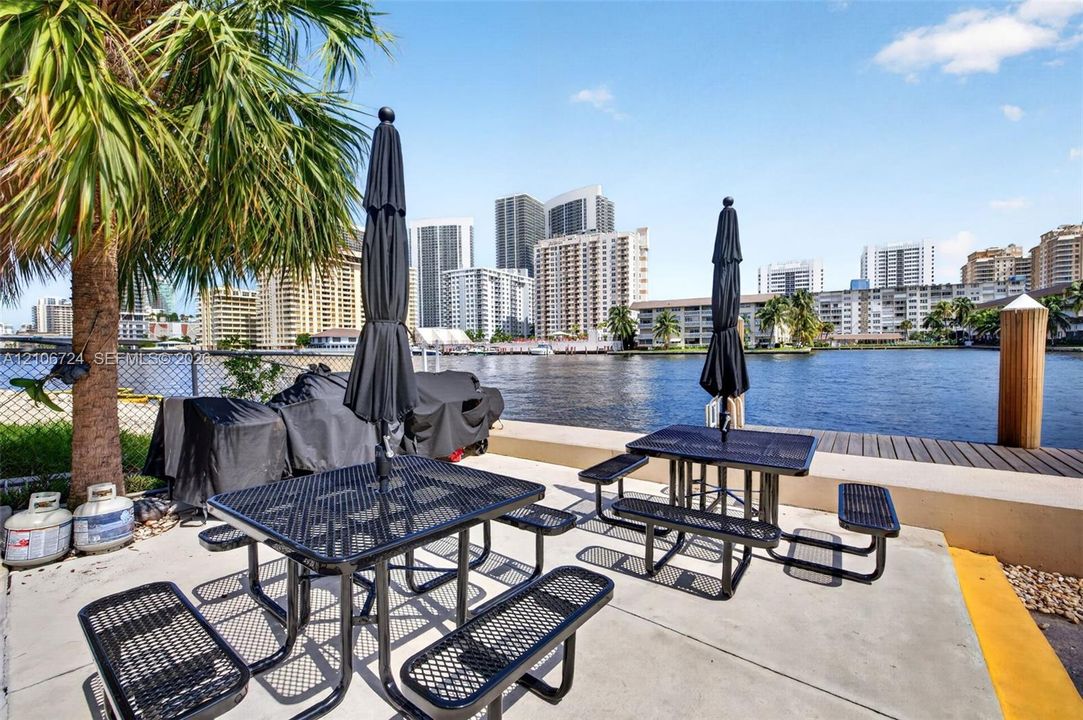 Waterfront patio area featuring concrete hardscaping, a fixed wooden piling, and a chain-link perimeter fence