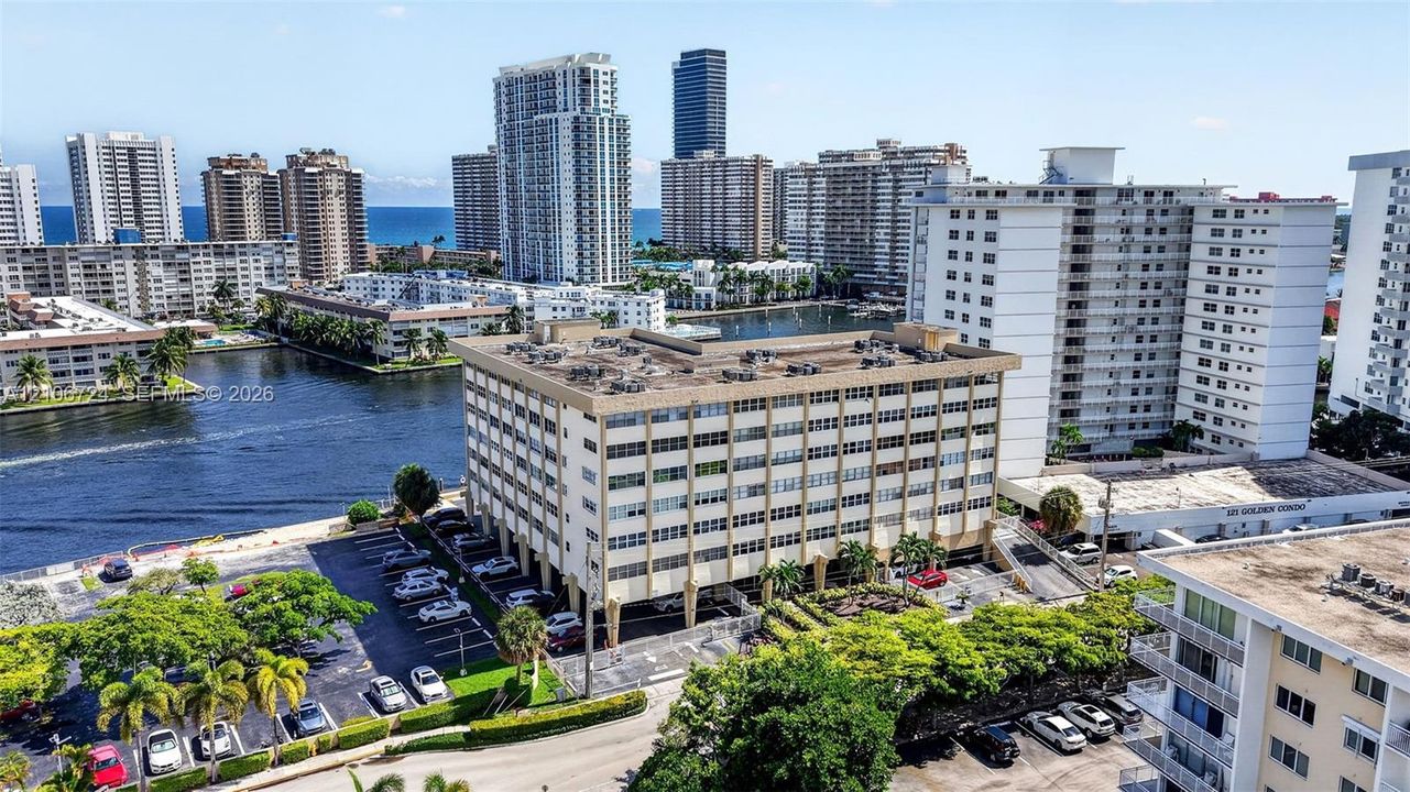 Aerial perspective of a multi-story residential building featuring covered ground-level parking, landscaped perimeter greenery, and direct water frontage along an inlet canal