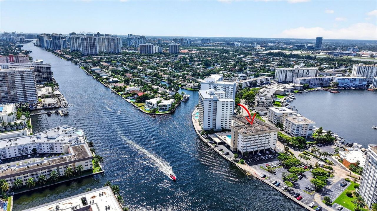 Aerial perspective of a waterfront mid-rise building featuring a swimming pool, asphalt parking area, and direct canal access