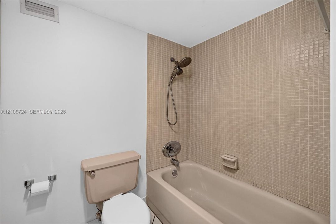 Bathtub with a shower head, tiled surround, and chrome hardware