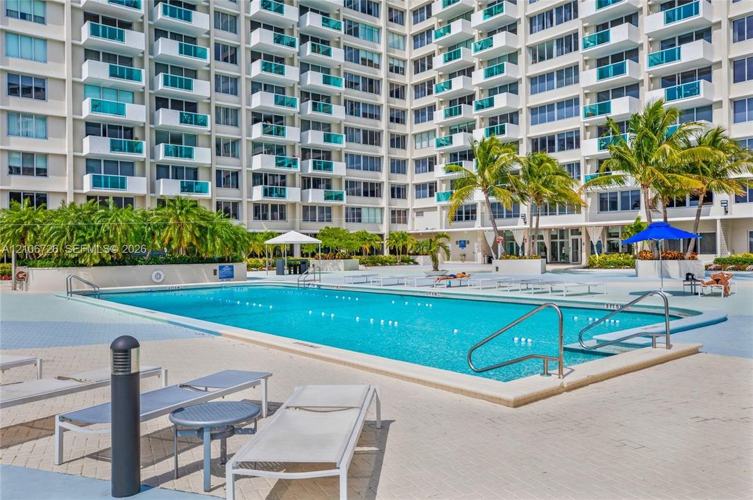 Swimming pool with metal handrails, paver pool deck, and integrated landscaping including palm trees