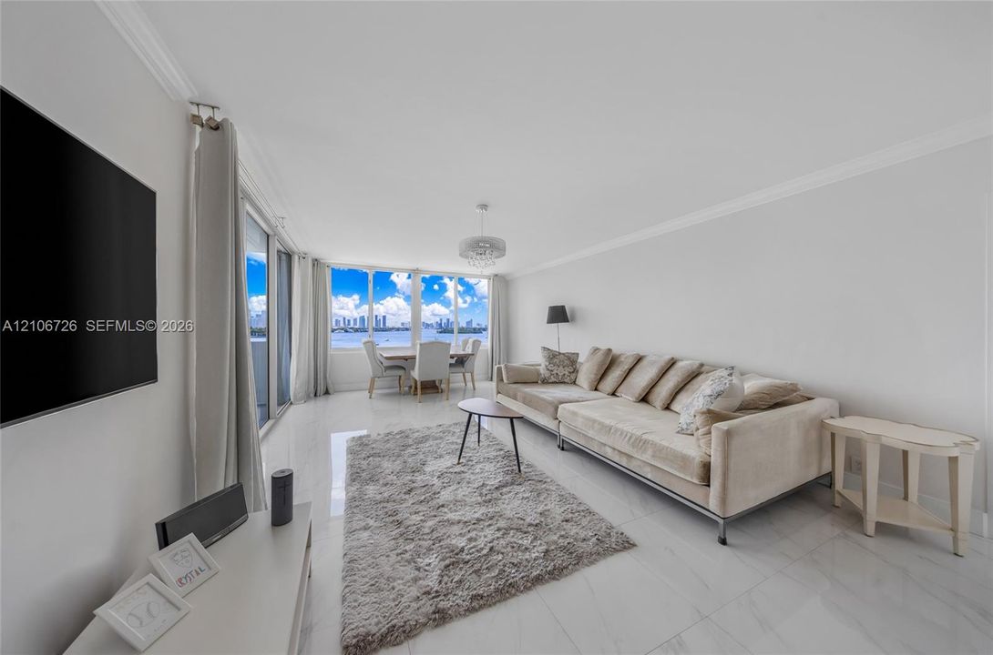 Open-concept living area featuring polished tile flooring, floor-to-ceiling windows, crown molding, and a drum-style ceiling light fixture