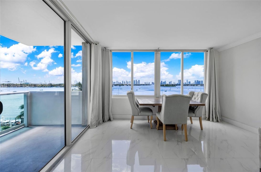 Floor-to-ceiling windows, polished stone-finish tile flooring, and sliding glass doors opening to a balcony with water and skyline scenery