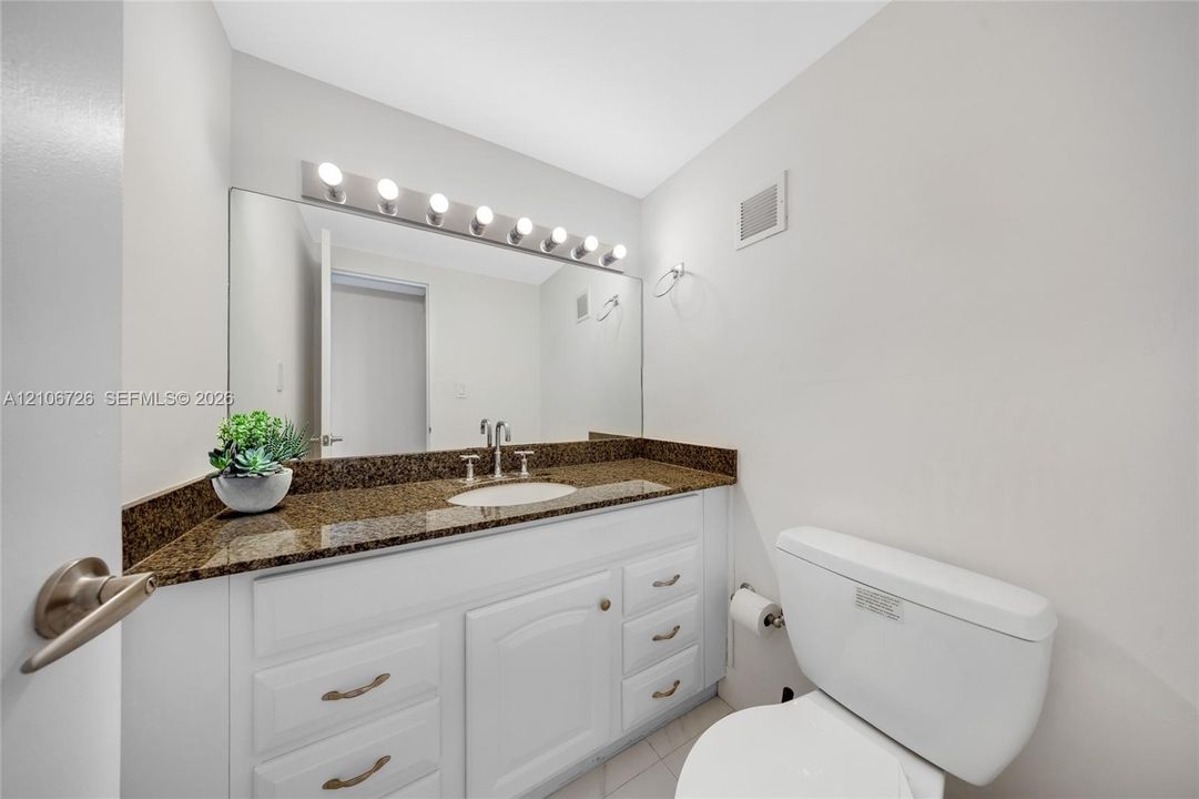Bathroom featuring a white vanity with multi-drawer storage, stone-finish countertop, integrated undermount sink, and full-width vanity mirror with integrated light fixture