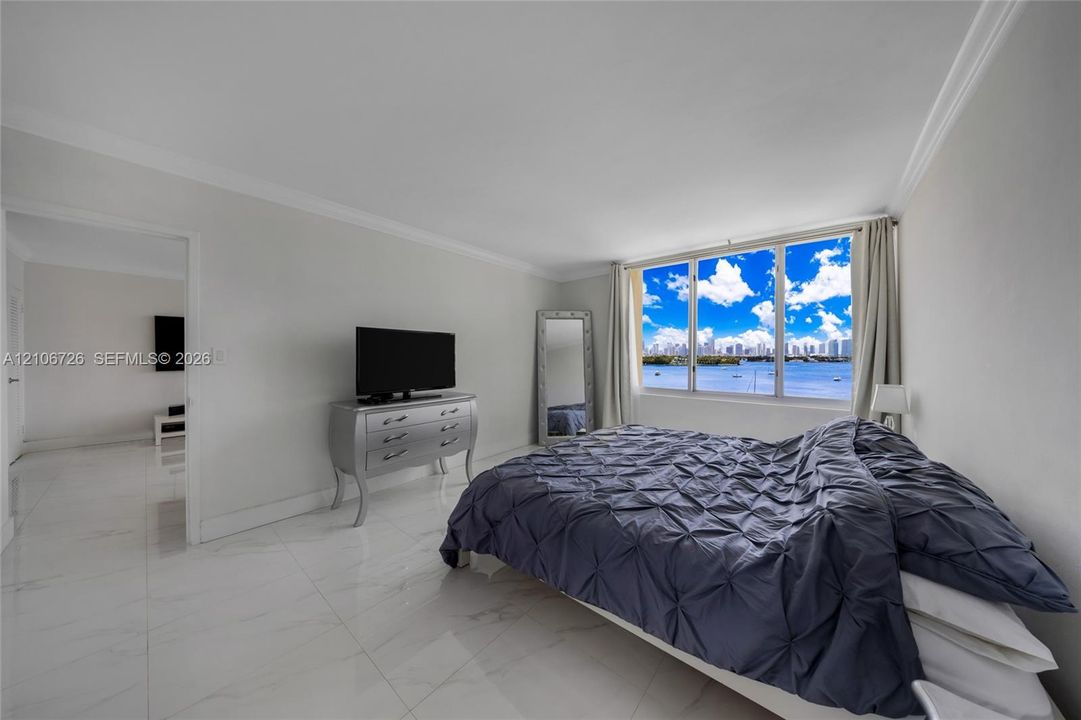 Interior space featuring polished white stone-finish flooring, crown molding, and expansive windows showcasing a water and skyline backdrop