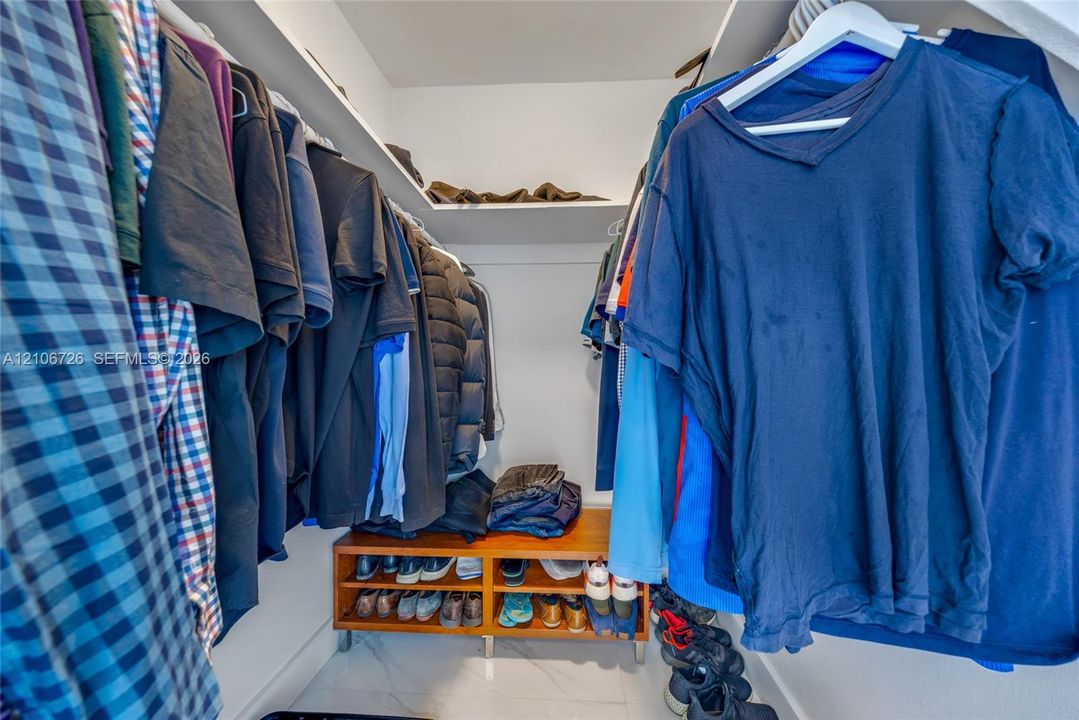 Walk-in closet featuring tiered shelving, built-in wooden storage unit, and polished tile flooring